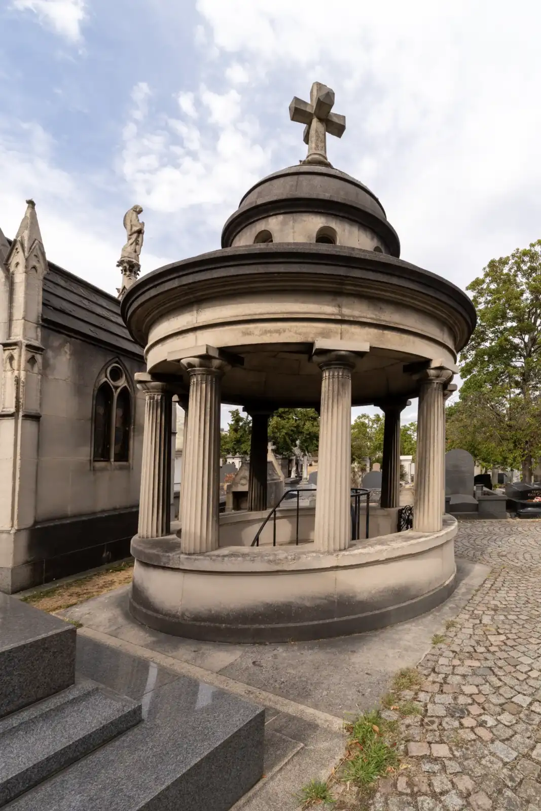 Une rotonde funéraire en pierre surmontée d'une croix dans un cimetière parisien.