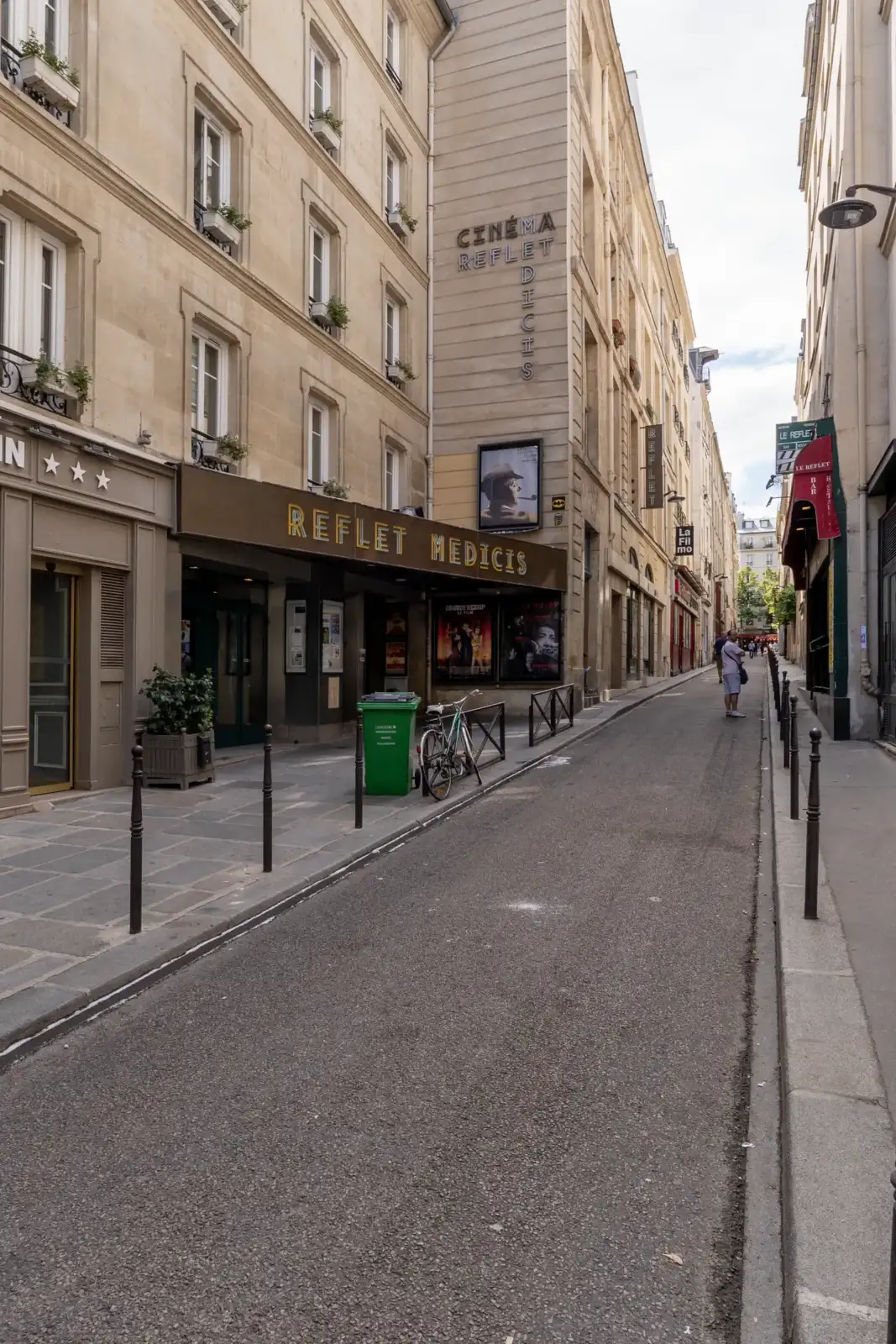 Vue de rue du cinéma Le Reflet Médicis à Paris, bordée d'immeubles haussmanniens.