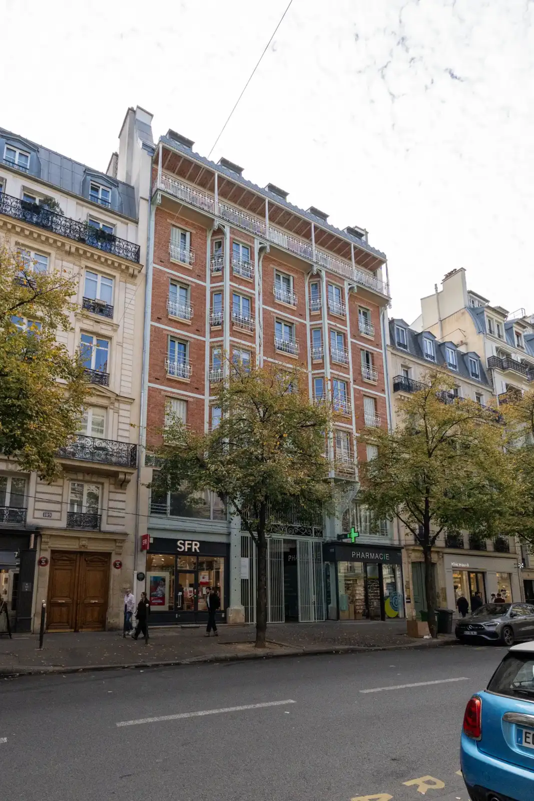 Une façade parisienne en briques et métal s'élève au-dessus de commerces animés.