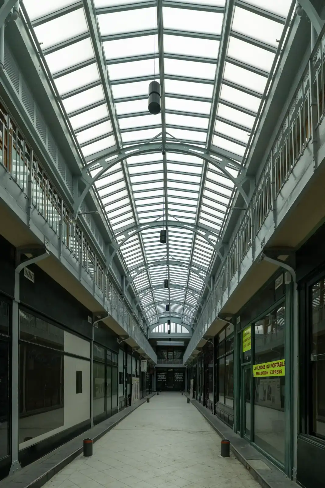 Une galerie couverte lumineuse de style verrière abrite des boutiques sous une structure métallique.