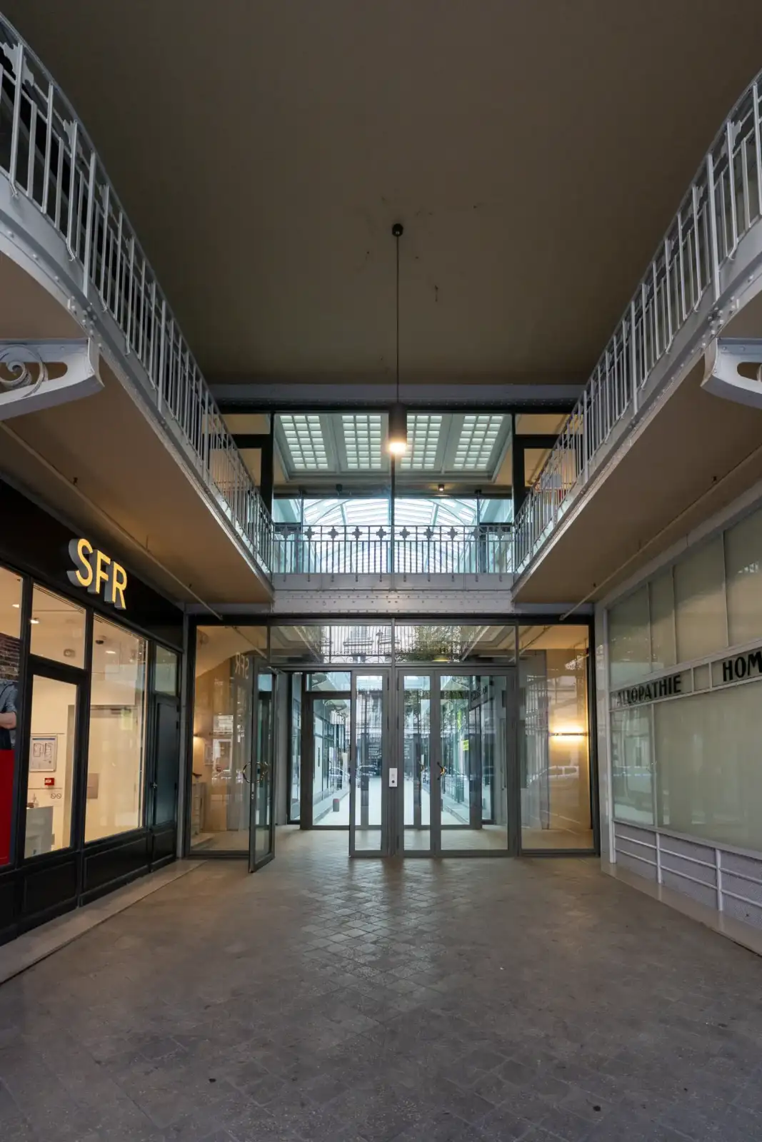 Vue intérieure d'une galerie marchande lumineuse avec des balcons en fer forgé.