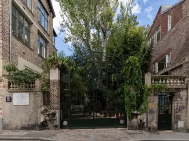 Grand portail en fer forgé verdoyant de la cité d'artistes La Ruche à Paris.