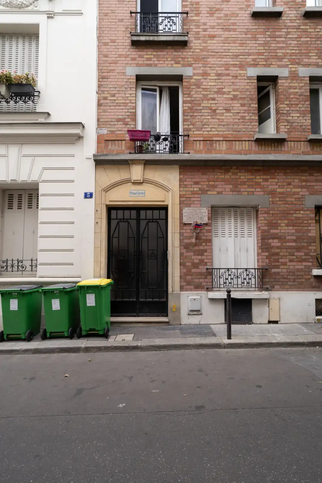 Façade en briques de la cité Falguière à Paris avec des poubelles vertes alignées.