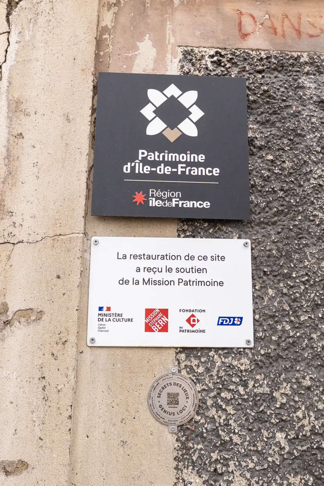 Un panneau officiel sur un mur abîmé indique le soutien à la restauration.