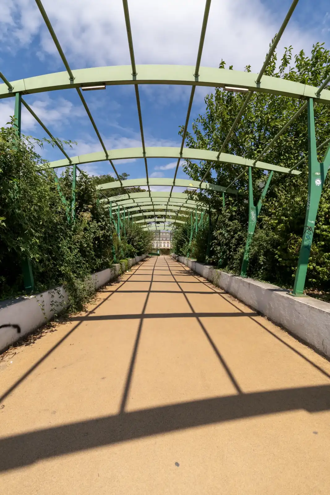Une allée ombragée à la Cité Internationale Universitaire de Paris avec une pergola métallique.