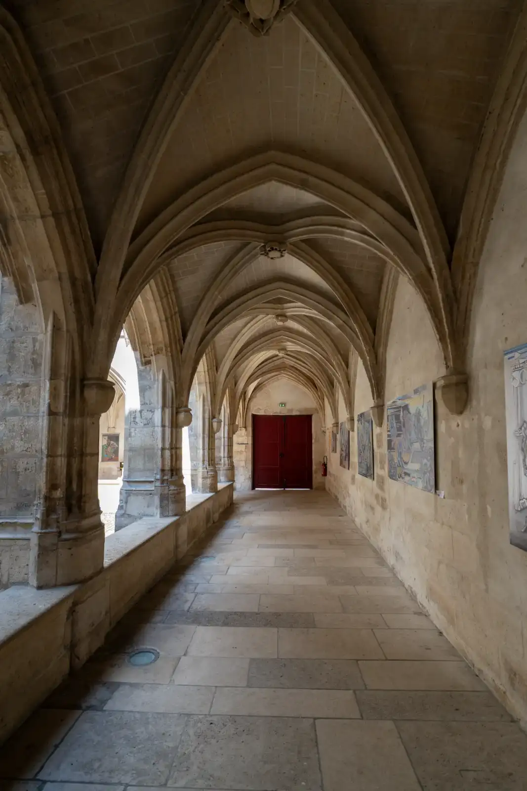 Vue en perspective du cloître voûté des Billettes, avec des œuvres exposées.