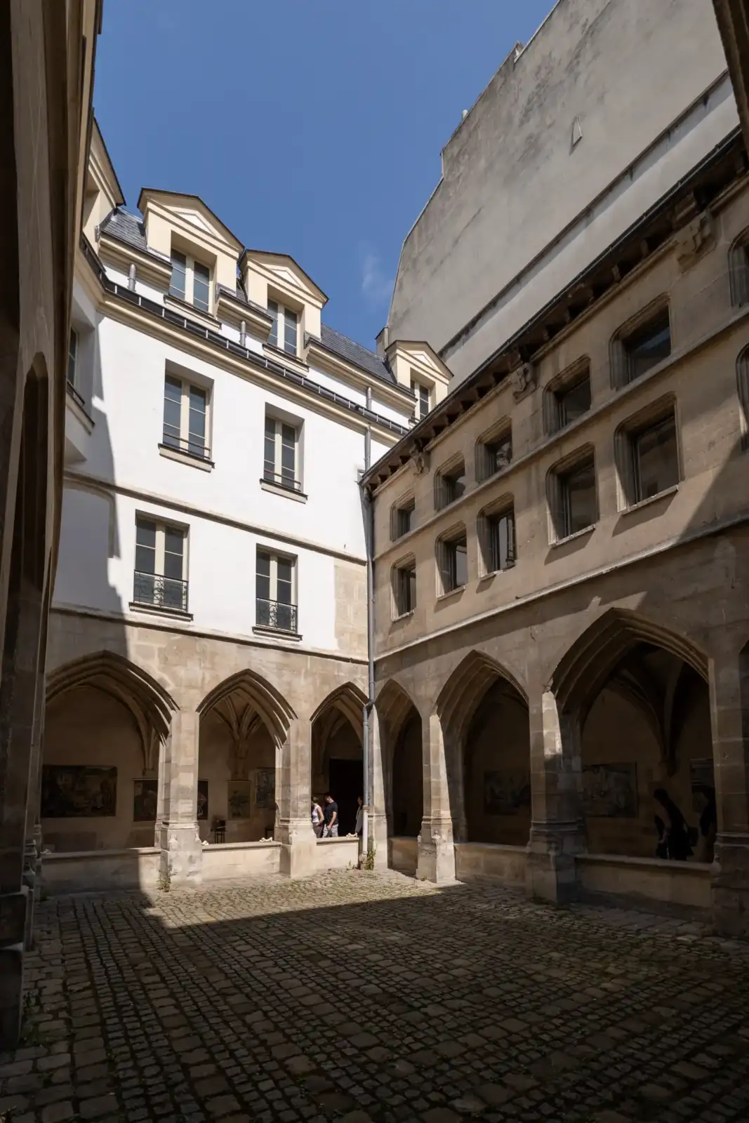 Une cour pavée entourée d'un cloître gothique et de façades historiques à Paris.