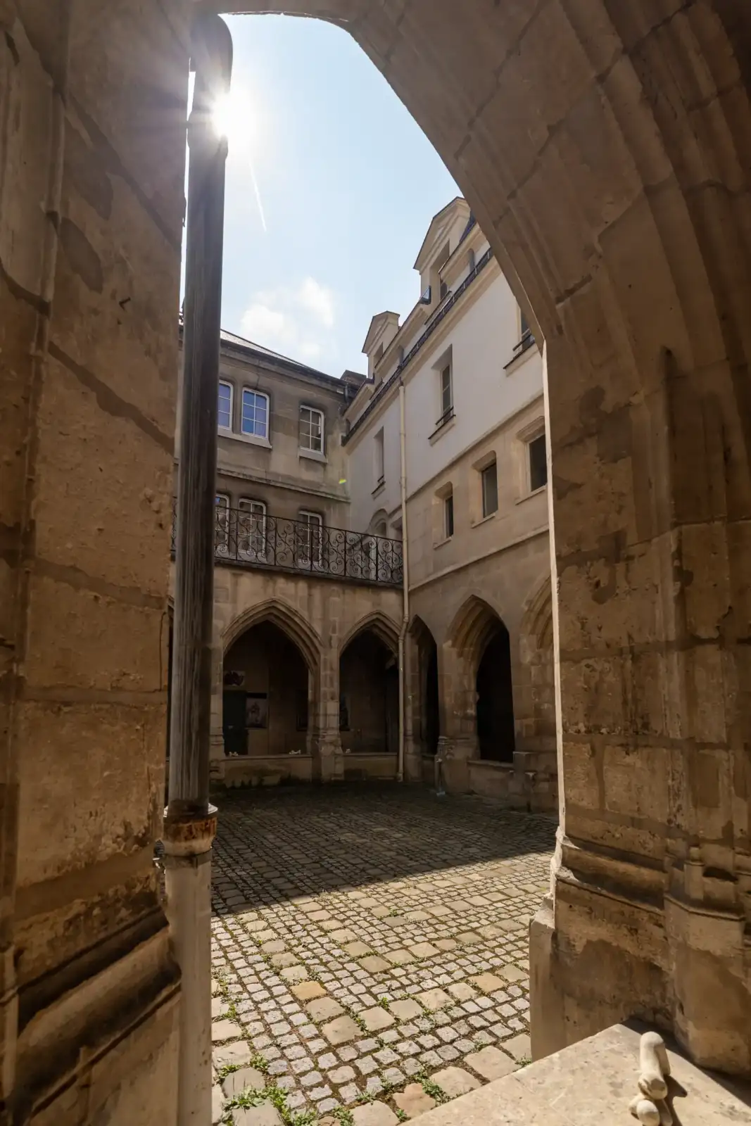 Vue en contre-plongée de la cour pavée du cloître des Billettes sous un beau soleil.