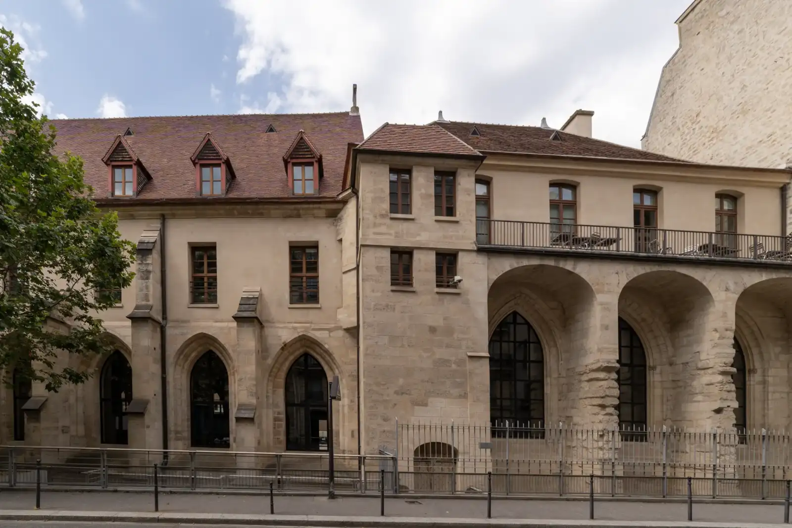 Façade médiévale en pierre du Collège des Bernardins avec de grandes arcades gothiques et des fenêtres à meneaux.