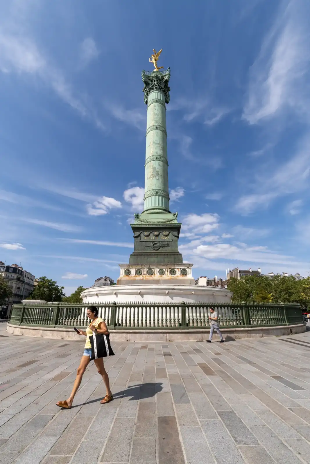 Une femme marche sur la place de la Bastille devant la haute colonne de Juillet.