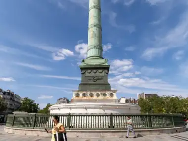 Une femme marche sur la place de la Bastille devant la haute colonne de Juillet.