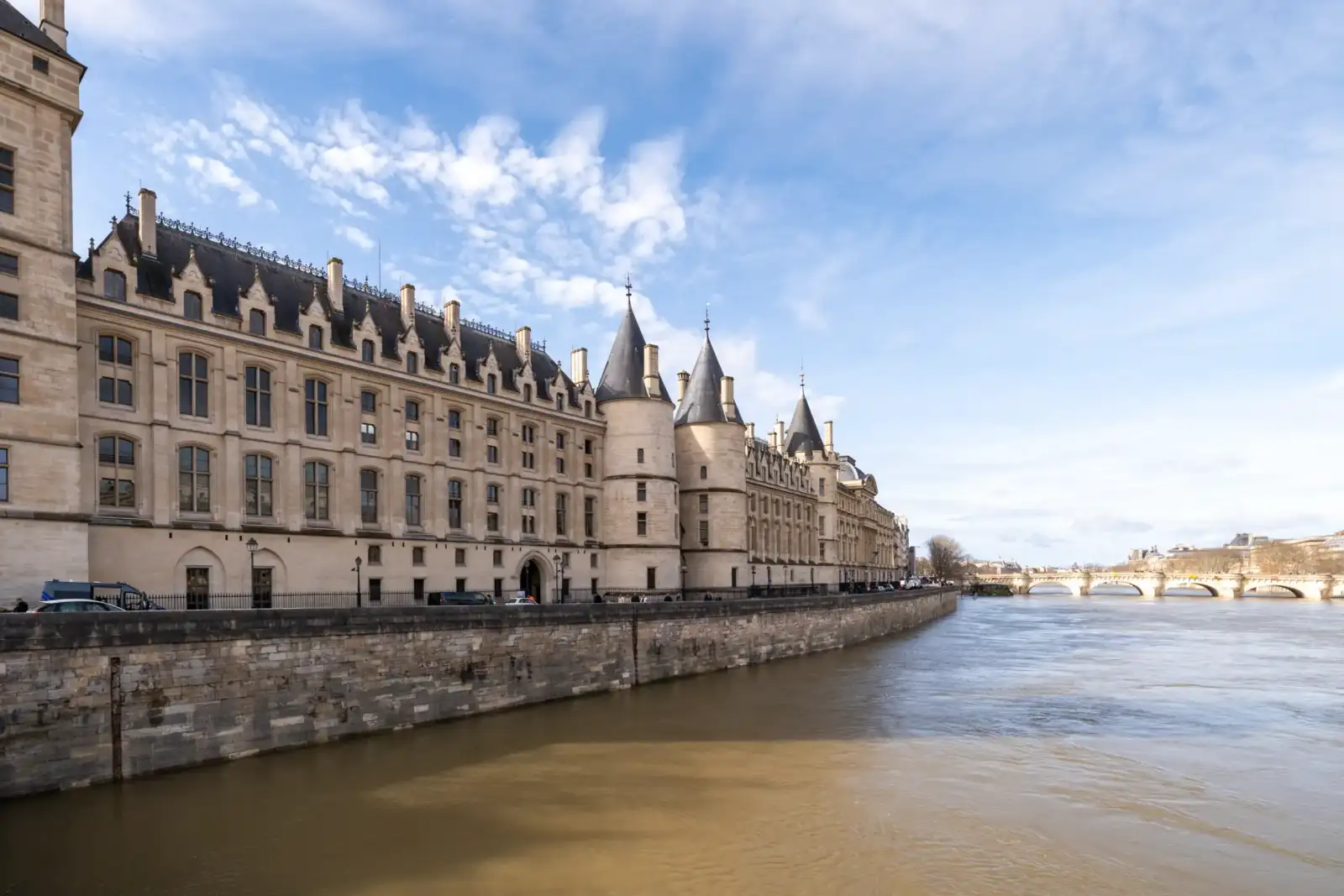 La façade historique de la Conciergerie borde la Seine sous un ciel bleu lumineux.
