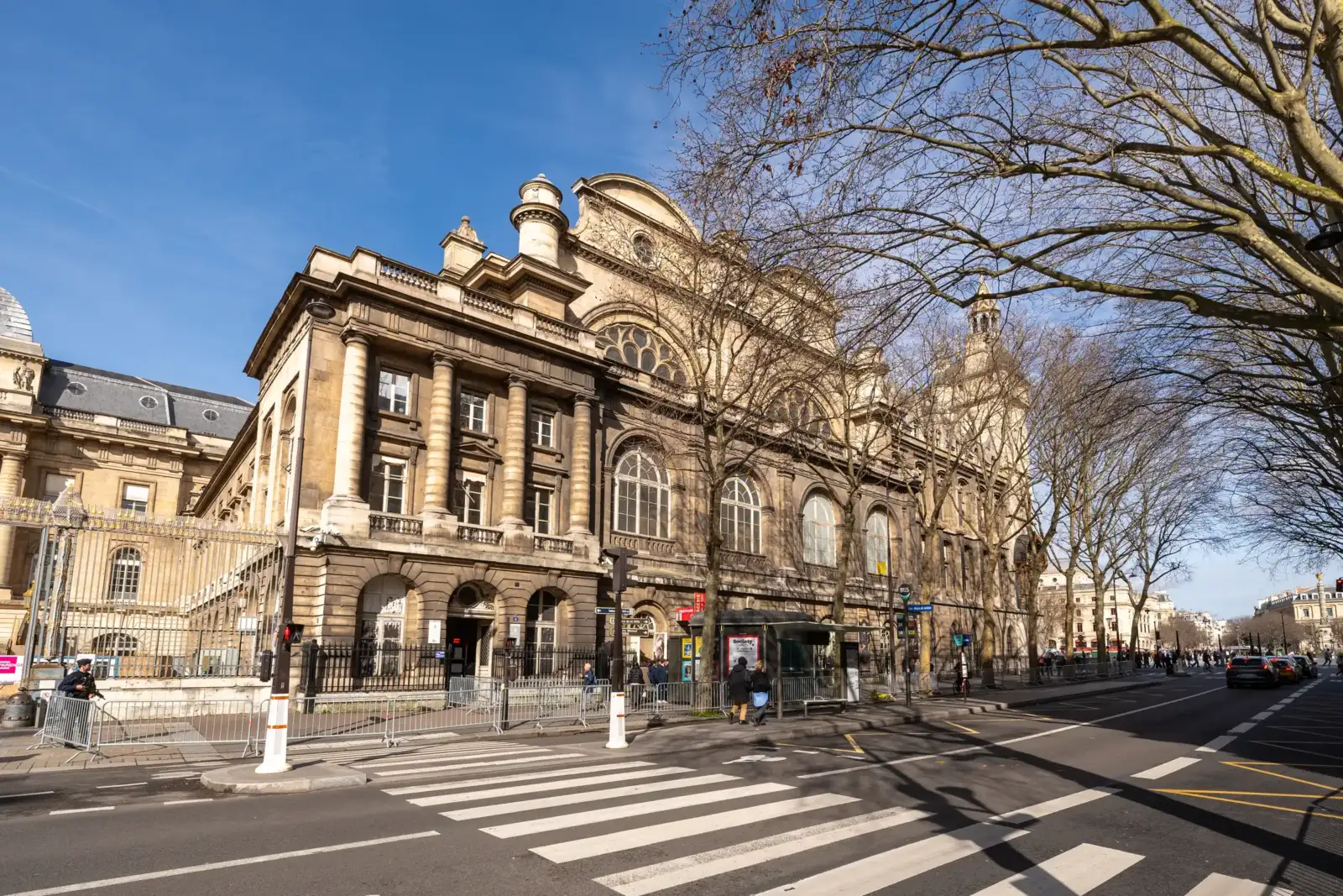 Vue de la façade historique de la Conciergerie depuis une rue parisienne ensoleillée.