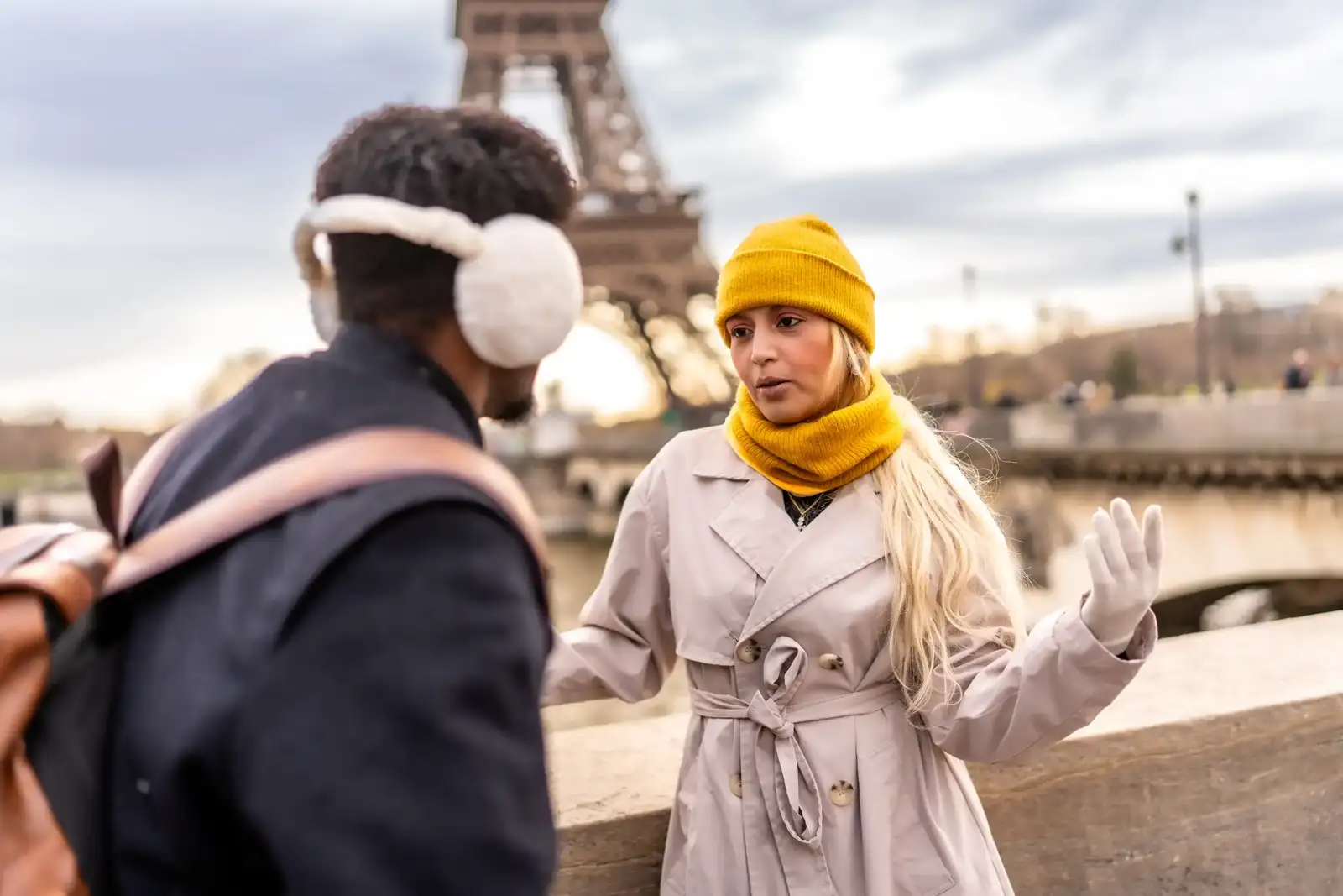 Un jeune couple discute en plein air à Paris avec la Tour Eiffel en arrière-plan.