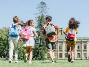 Quatre écoliers avec des sacs à dos courent joyeusement dans un parc ensoleillé.
