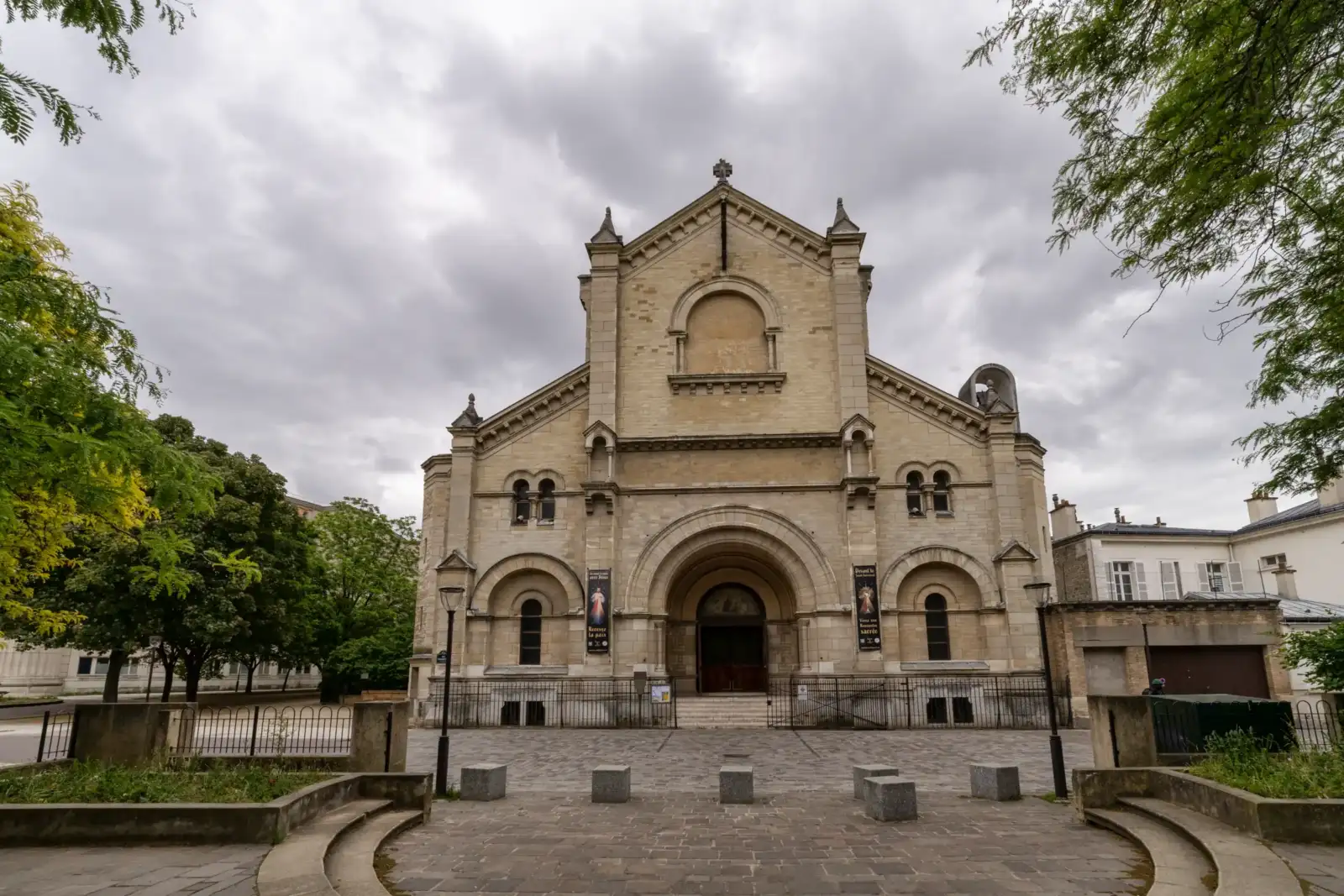 Façade en pierre de l’église Notre-Dame-du-Travail à Paris sous un ciel nuageux.