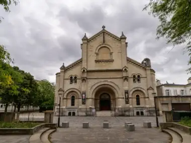 Façade en pierre de l’église Notre-Dame-du-Travail à Paris sous un ciel nuageux.