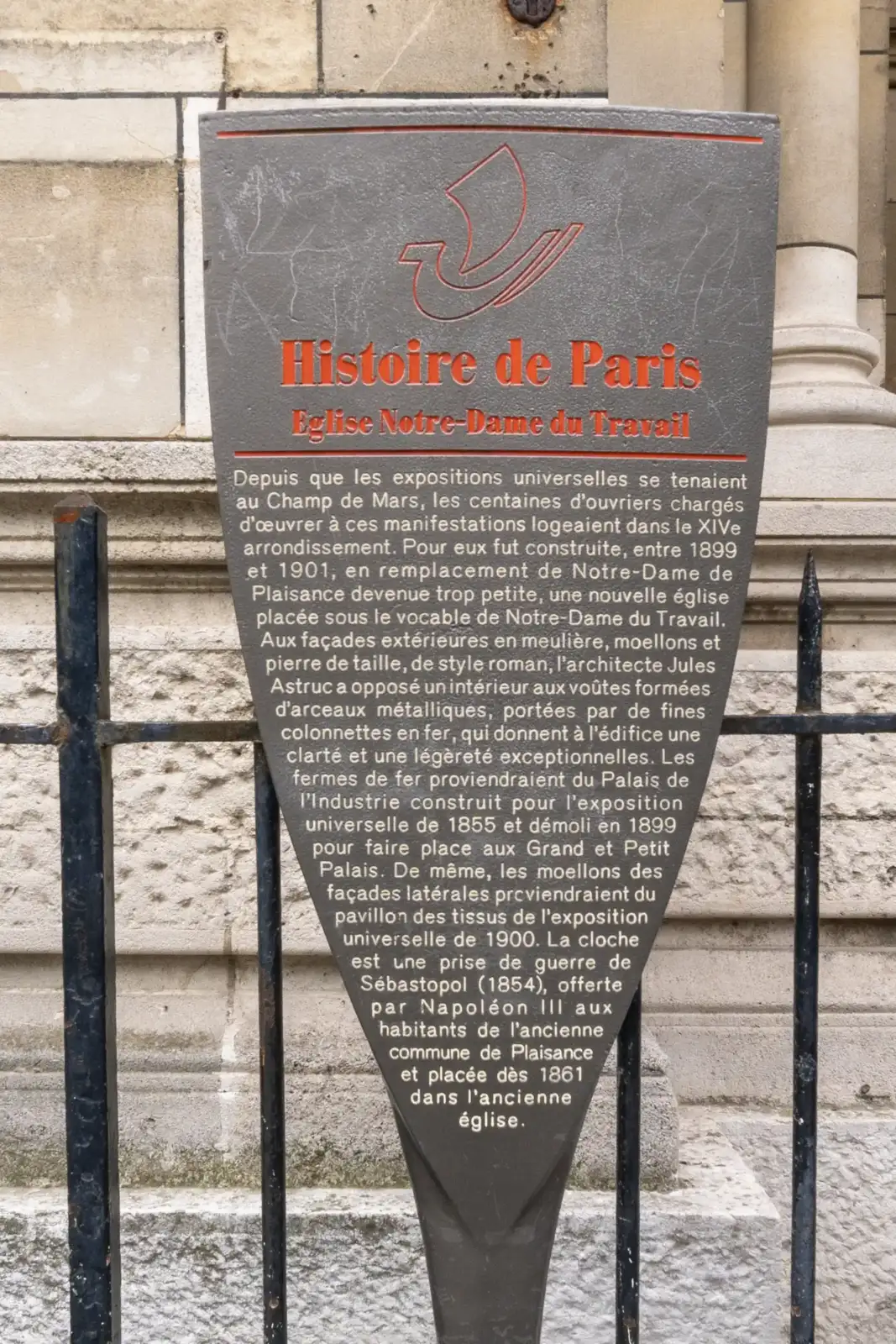 Un panneau d'information historique en métal gris raconte l'église Notre-Dame du Travail.