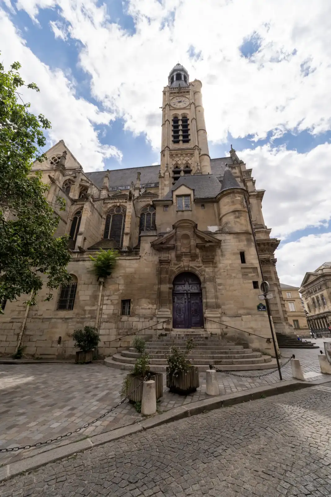 Vue en contre-plongée de la façade gothique de l'église Saint-Étienne-du-Mont à Paris, sous un ciel nuageux.