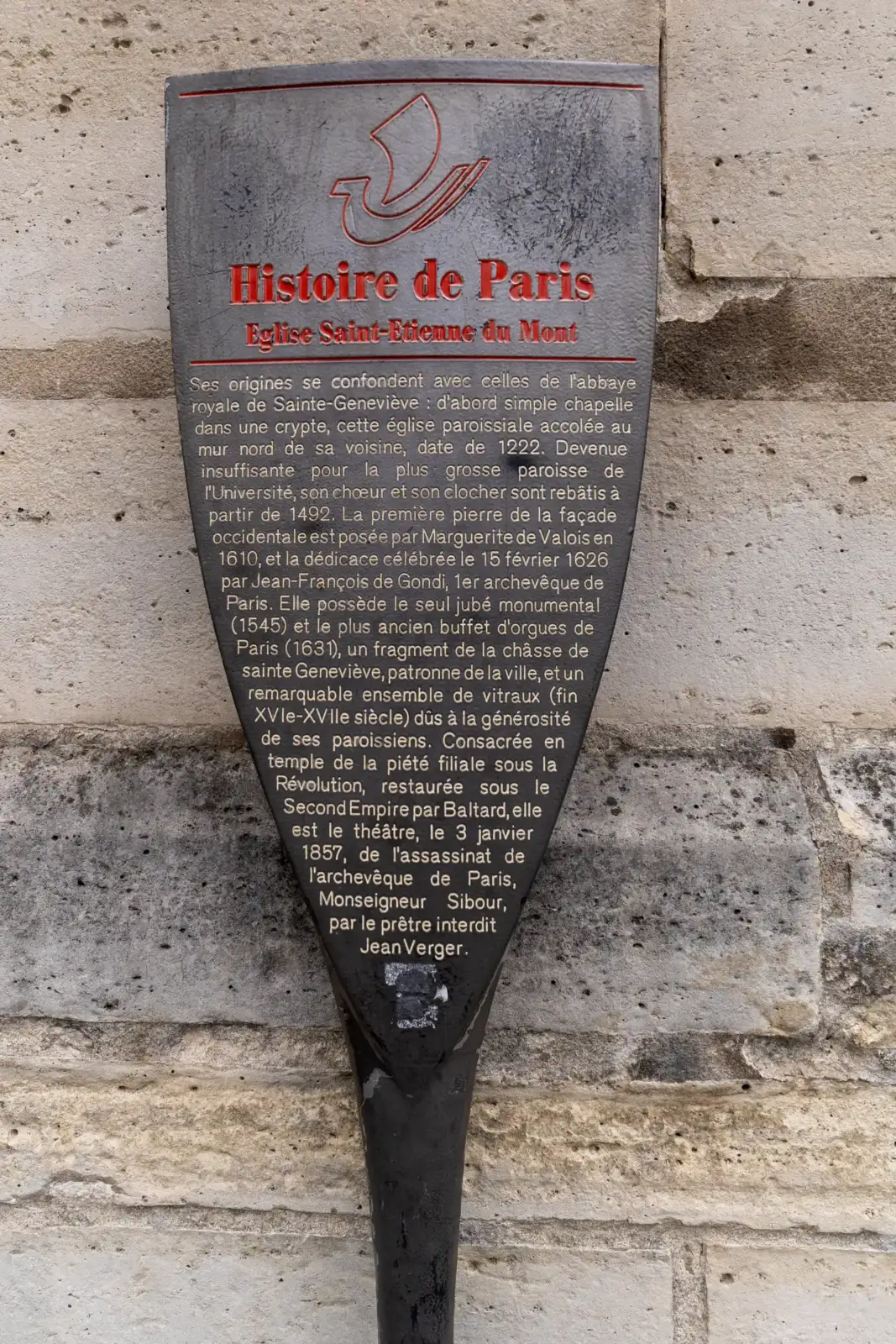 Un panneau informatif sombre et texturé est fixé sur un mur en pierre calcaire.