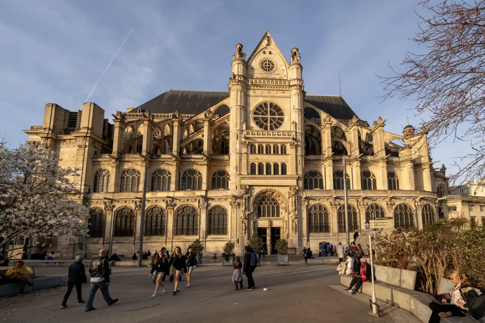 La façade gothique de l'église Saint-Eustache domine une place parisienne animée sous le soleil.