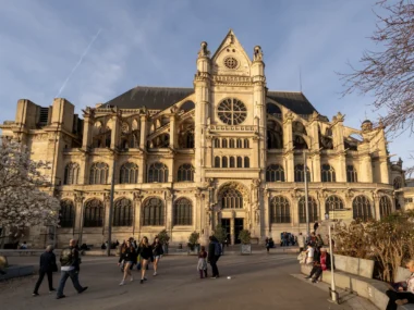 La façade gothique de l'église Saint-Eustache domine une place parisienne animée sous le soleil.