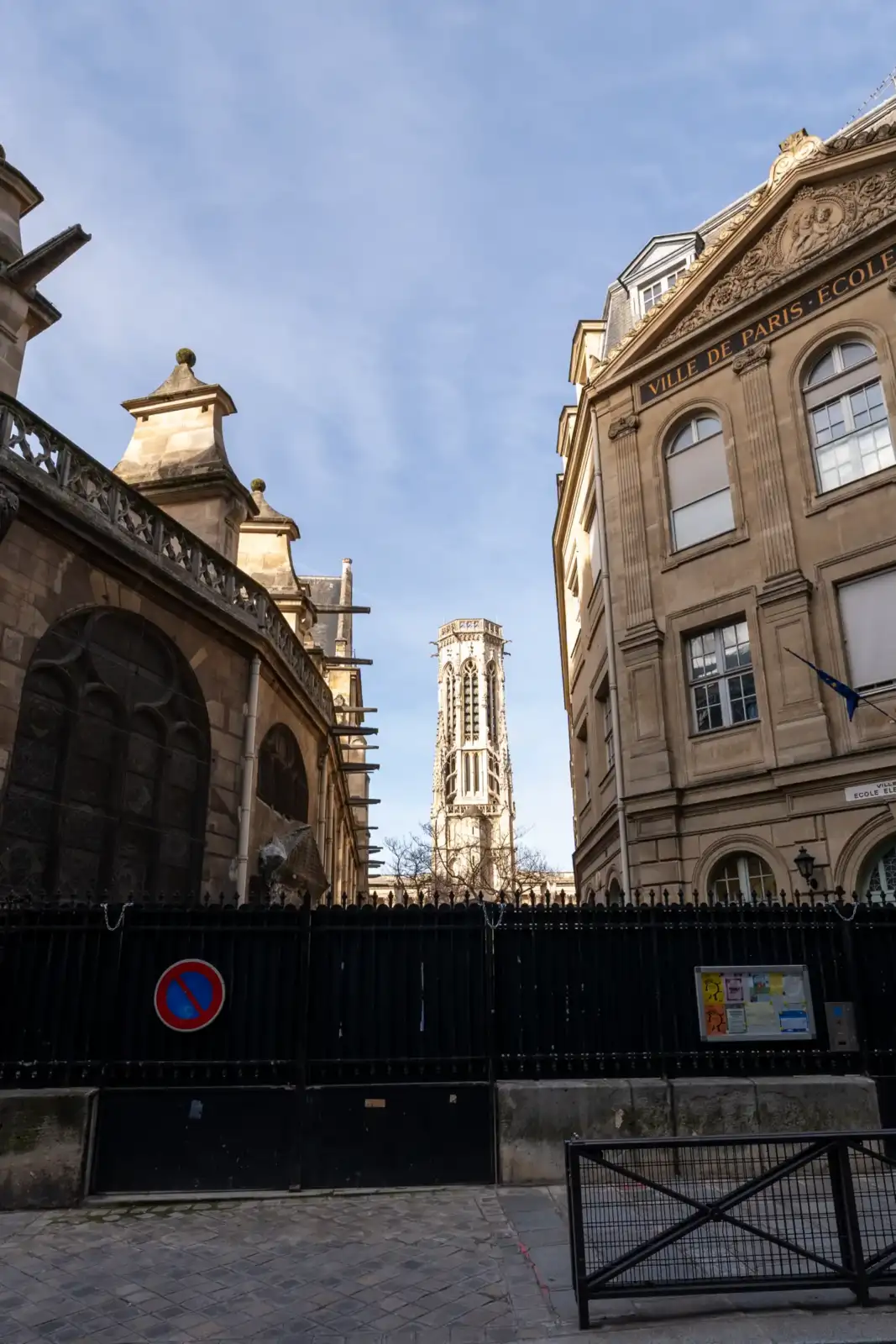 La tour de l'église Saint-Germain-l'Auxerrois s'élève entre deux bâtiments parisiens sous un ciel bleu.