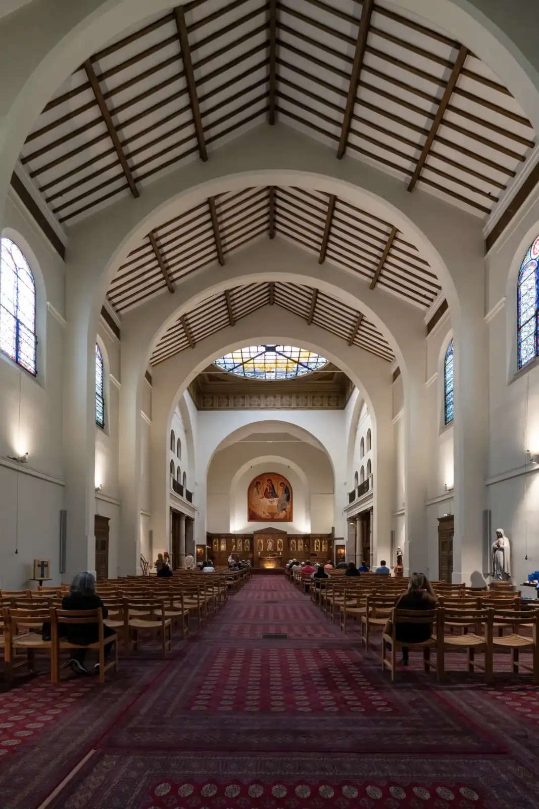 Vue intérieure de l'église Saint Honore Eylau avec un long tapis rouge et des fidèles assis sur des chaises en bois.
