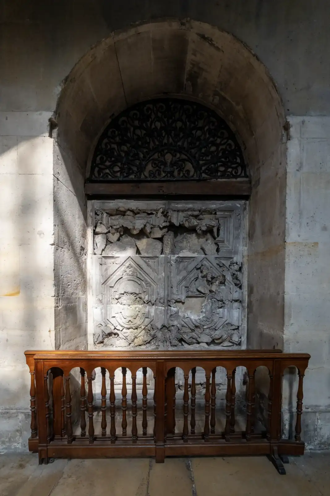 Une porte en bois abîmée se trouve sous une arche de pierre avec balustrade.