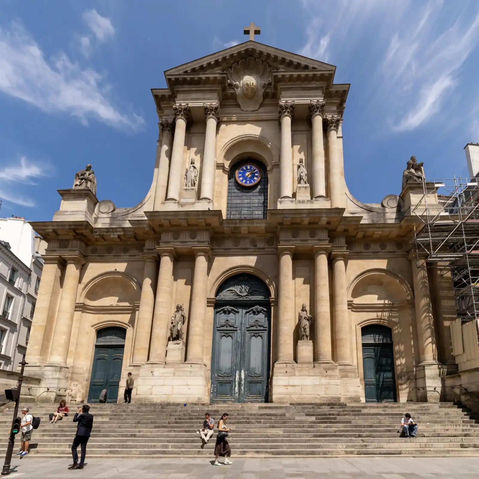 Vue de face de l'église Saint-Roch à Paris, sous un ciel bleu lumineux.