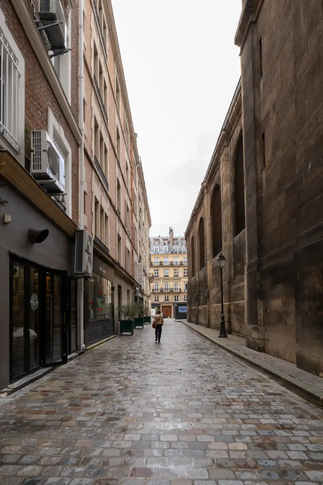 Une personne marche dans une rue pavée étroite bordée par l'église Saint-Roch à Paris.