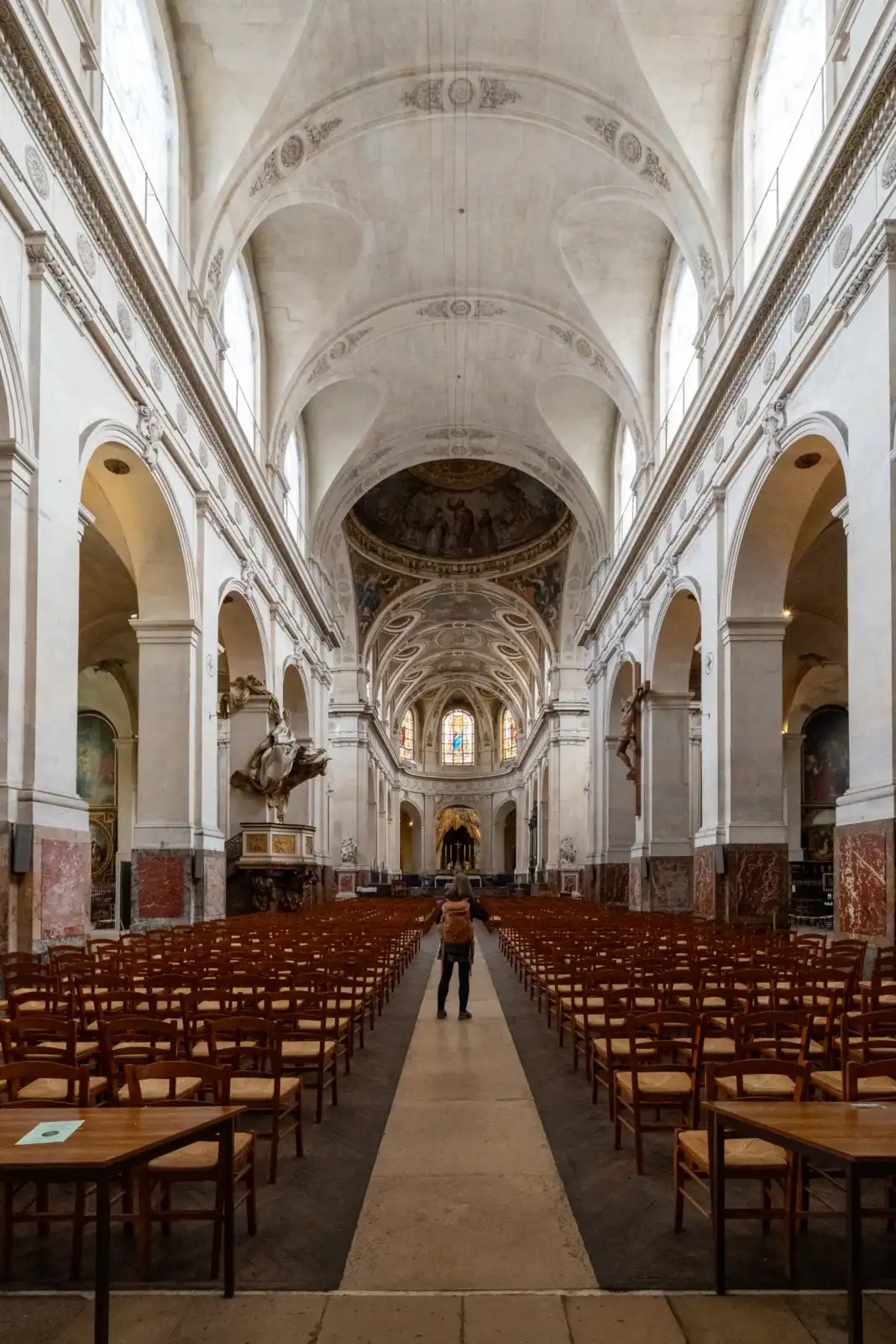 Une personne debout dans l'allée centrale de l'église Saint-Roch entourée de chaises en bois.