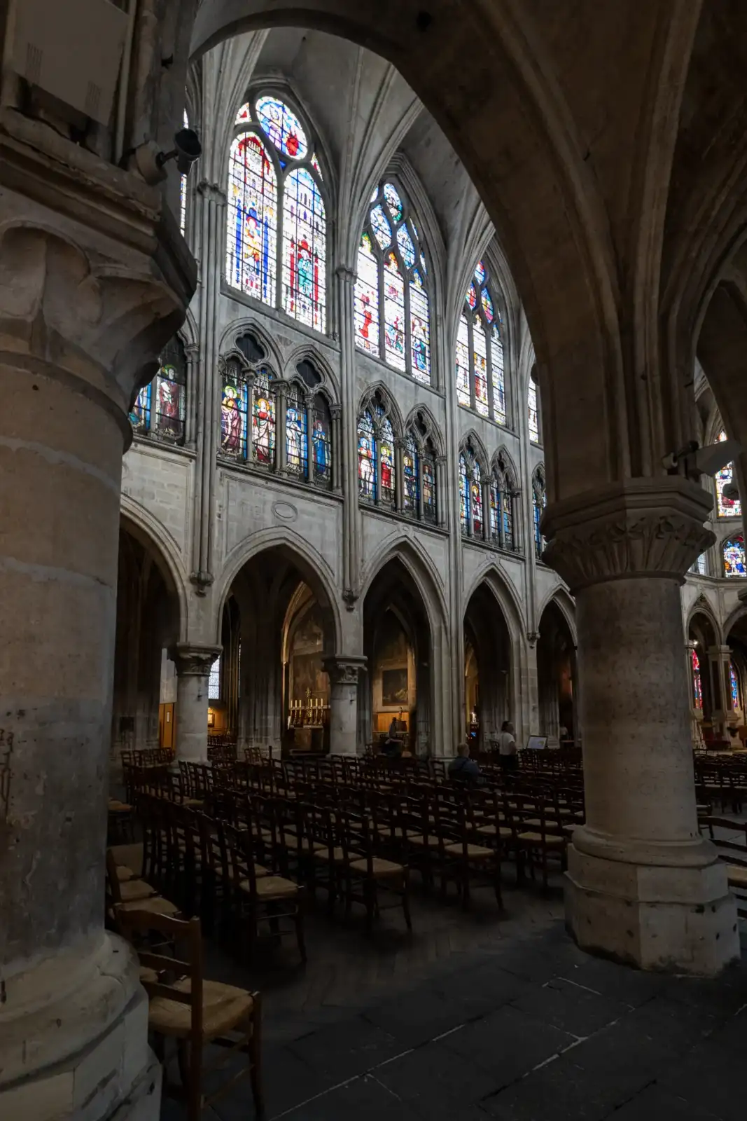 Vue intérieure de l église Saint Séverin à Paris montrant des rangées de chaises en bois et des vitraux lumineux.