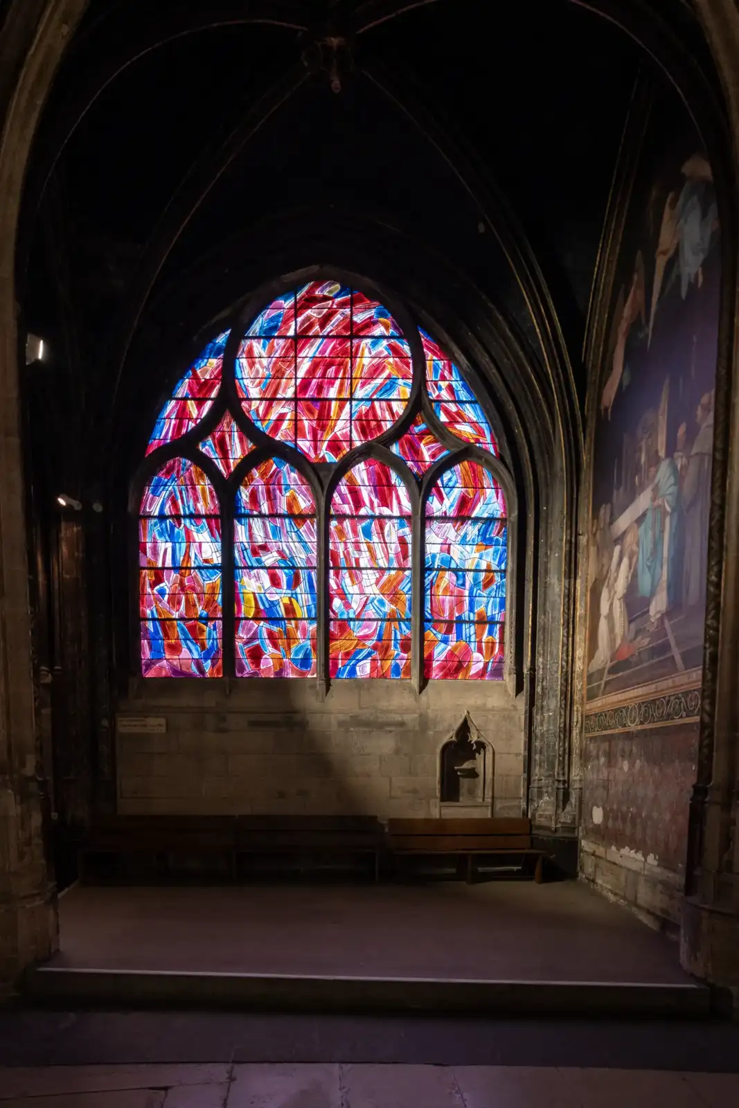 Vue intérieure de l église Saint Séverin illuminée par un grand vitrail coloré.
