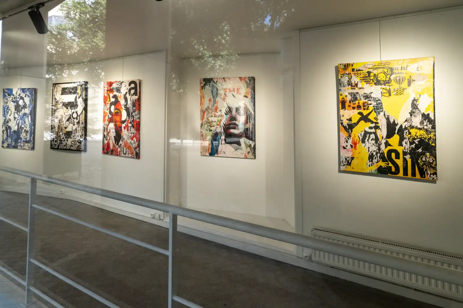 Une exposition de tableaux colorés contemporains est visible à travers une vitre transparente lumineuse.