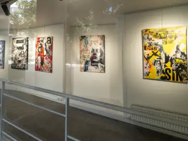 Une exposition de tableaux colorés contemporains est visible à travers une vitre transparente lumineuse.