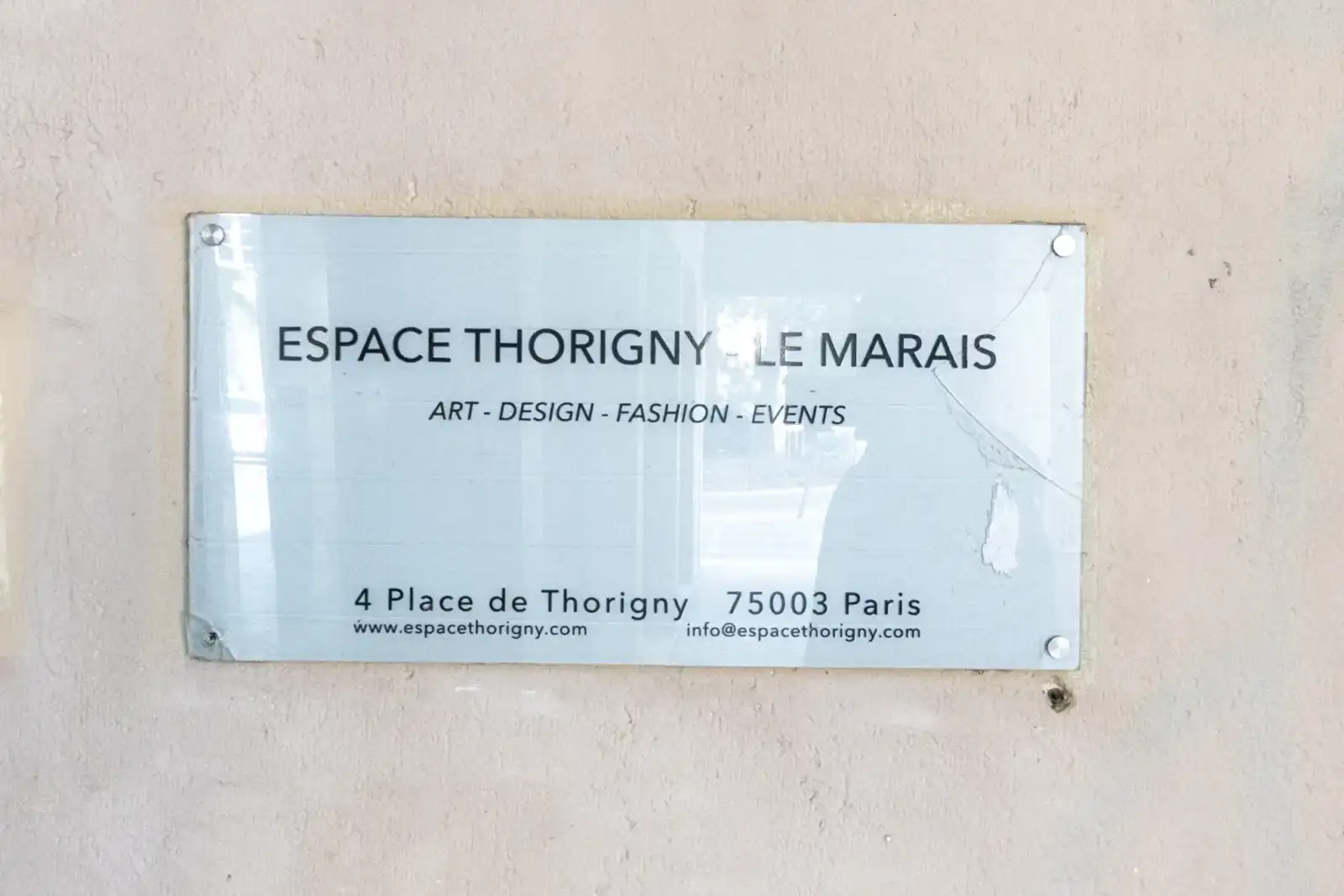 Une plaque transparente fixée sur un mur beige indique Espace Thorigny Le Marais.
