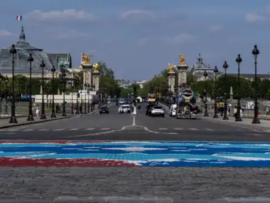 Une rue animée de Paris mène au Pont Alexandre III et au Grand Palais sous le soleil.
