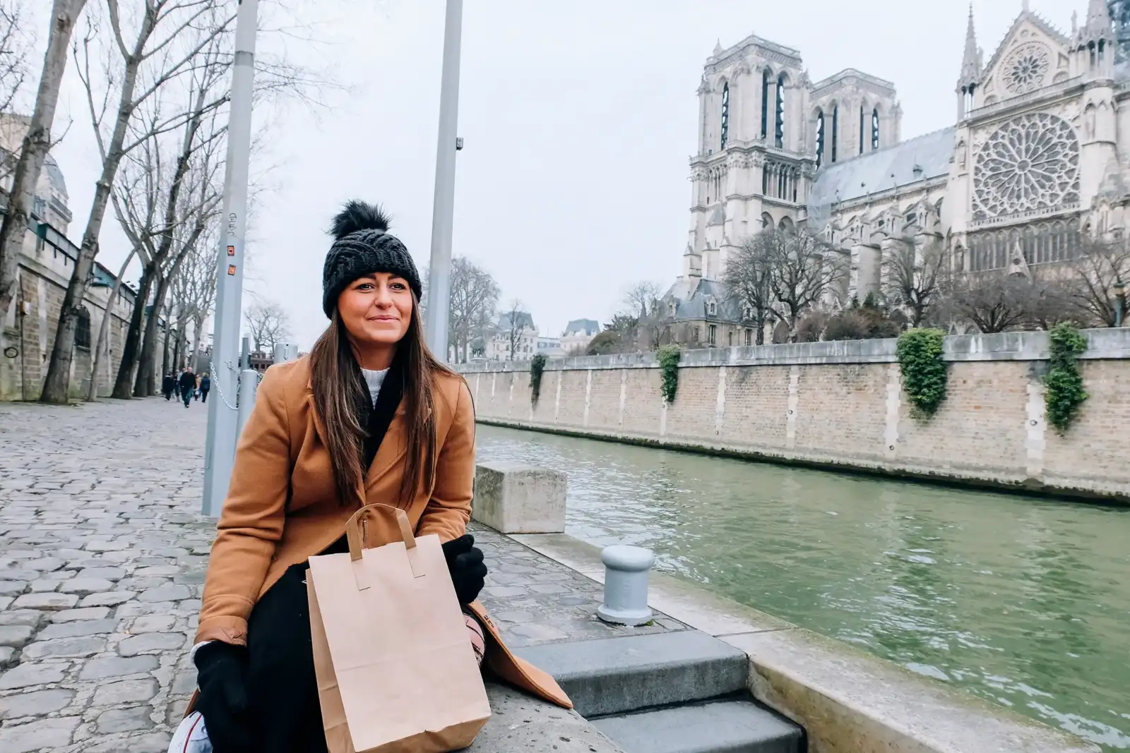 Une femme en manteau et bonnet pose sur les quais de Seine à Paris.