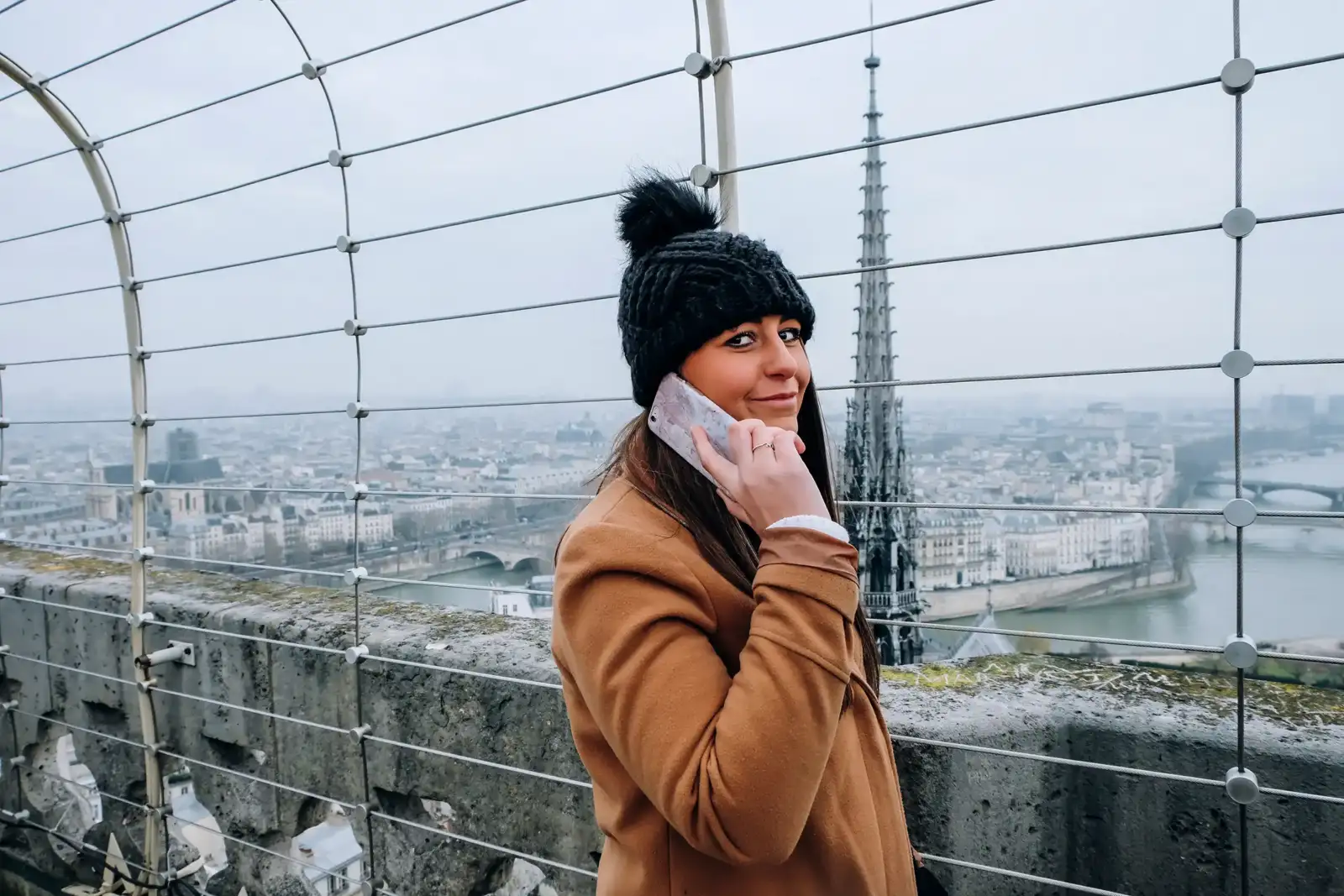 Une femme téléphone devant un panorama de Paris un jour de novembre.