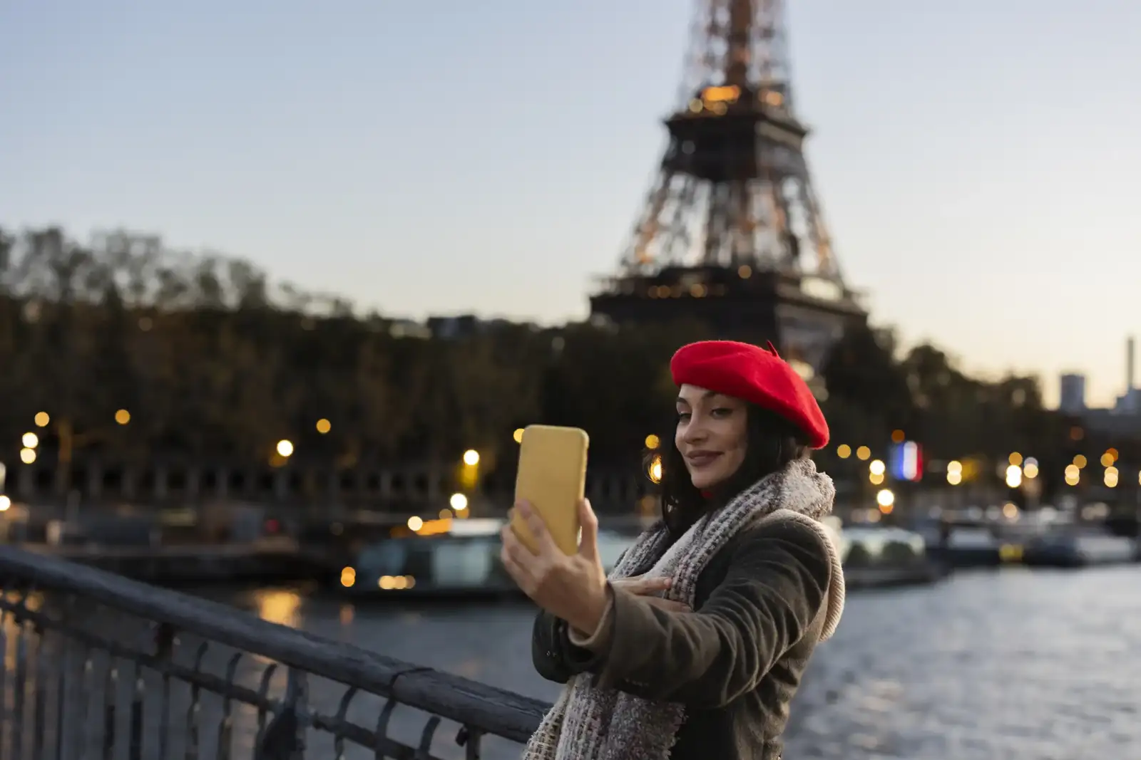 Une femme en béret rouge prend un selfie au bord de la Seine.