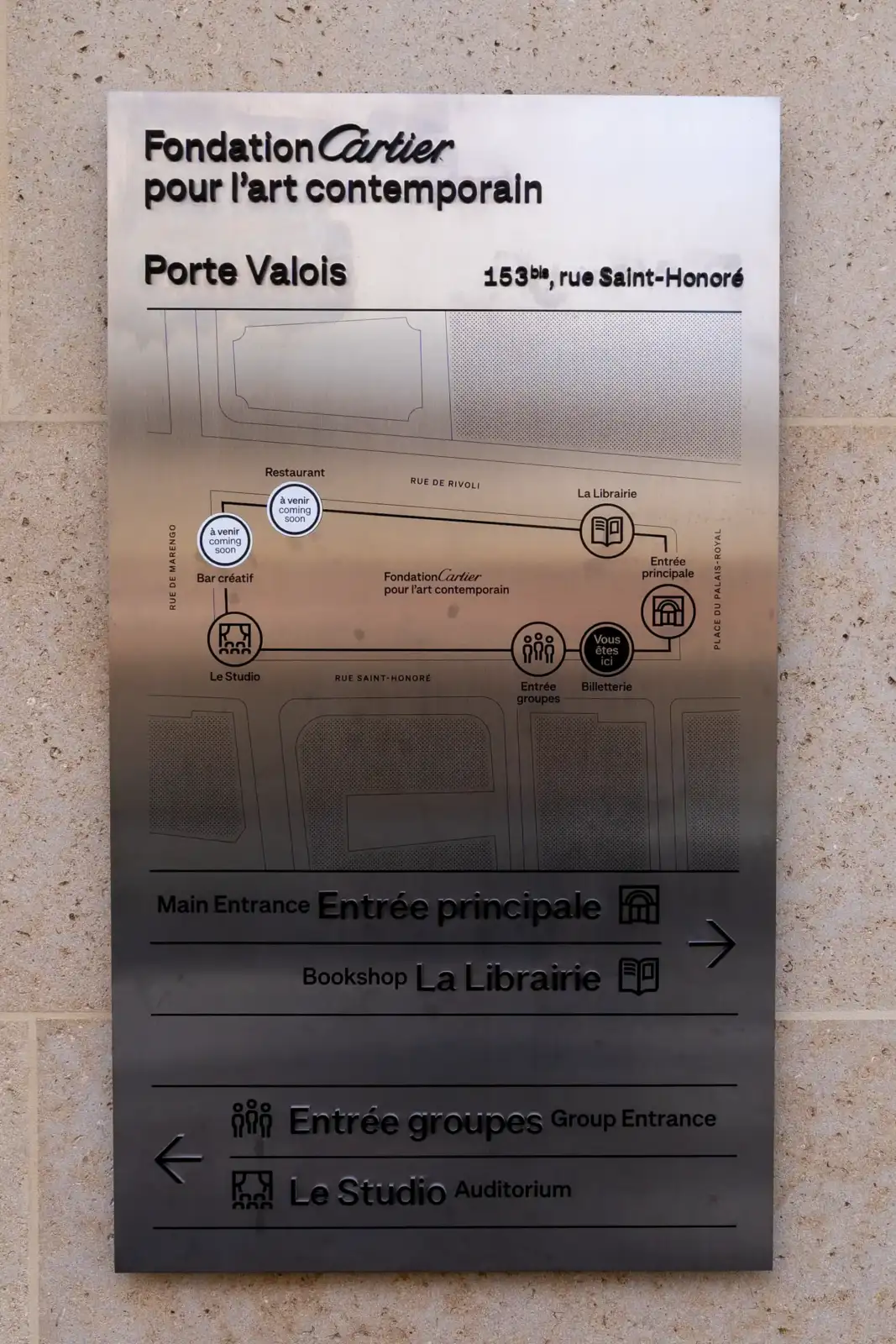 Panneau signalétique métallique de la Fondation Cartier fixé sur un mur en pierre beige.