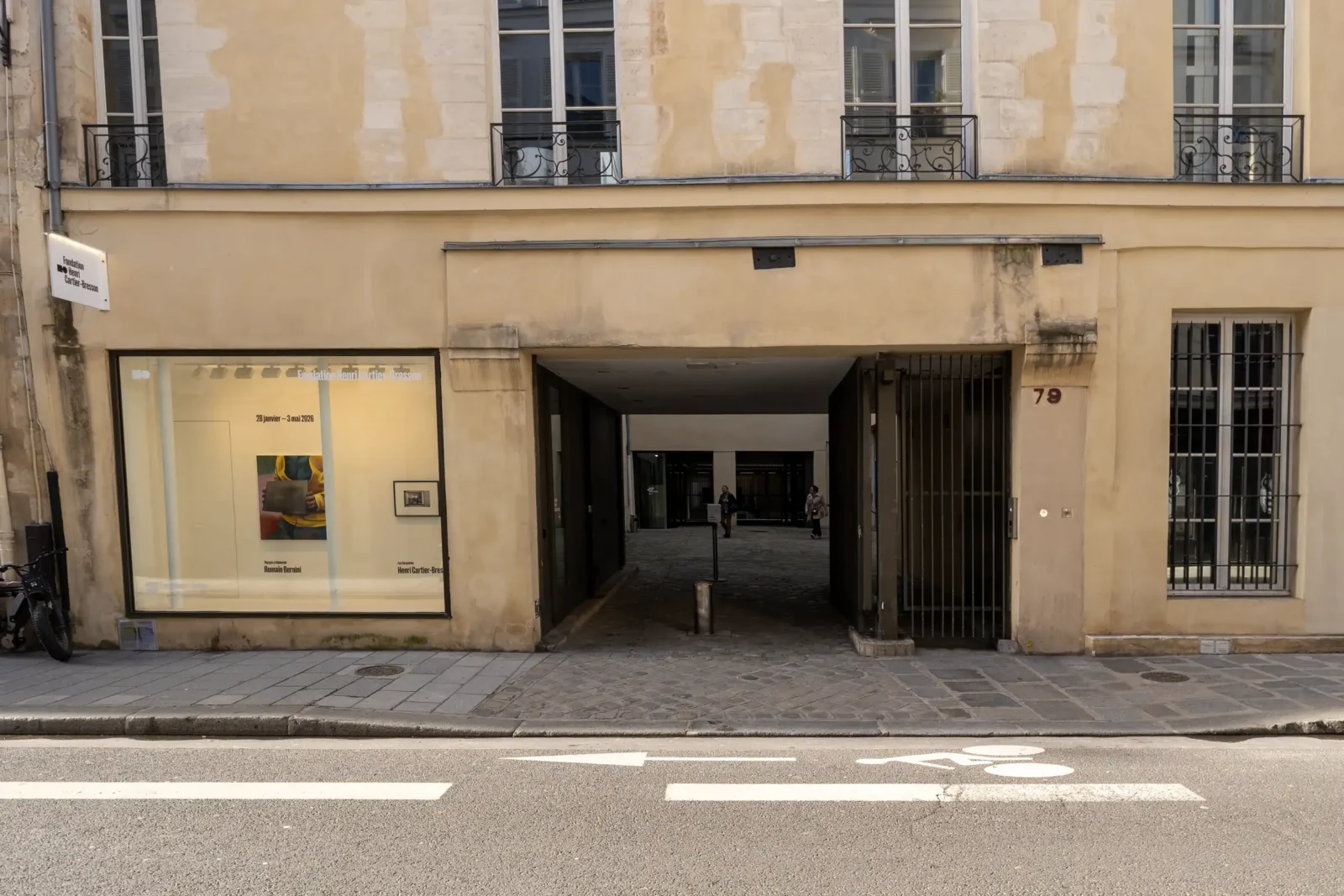 Façade beige de la Fondation Henri Cartier-Bresson avec une entrée voûtée et vitrine éclairée.