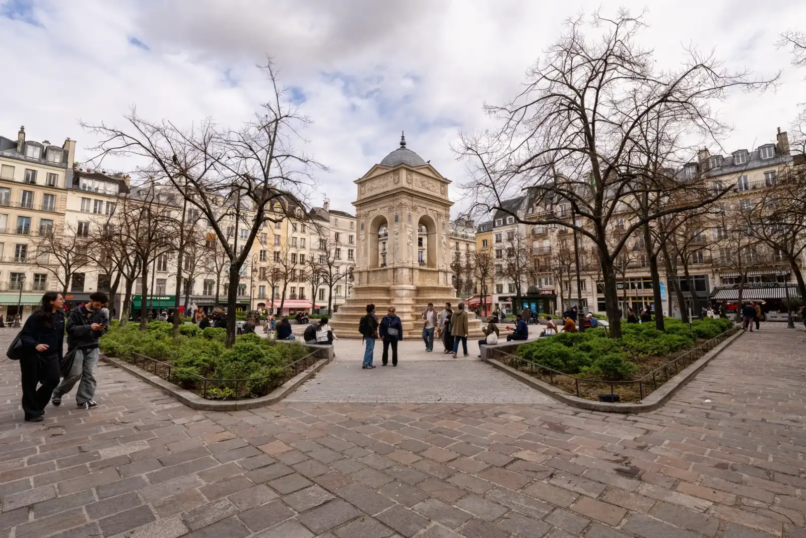 La fontaine des Innocents trône au centre d'une place parisienne entourée d'arbres dénudés.