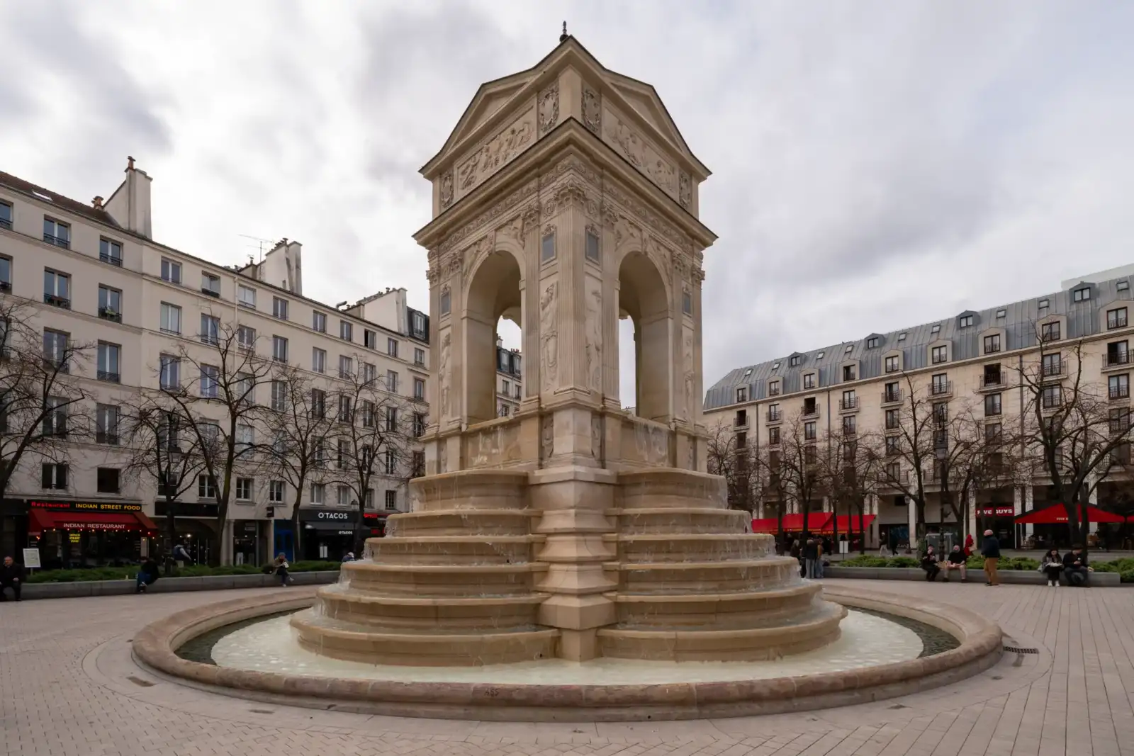 La fontaine des Innocents se dresse au centre d une place parisienne sous ciel gris.