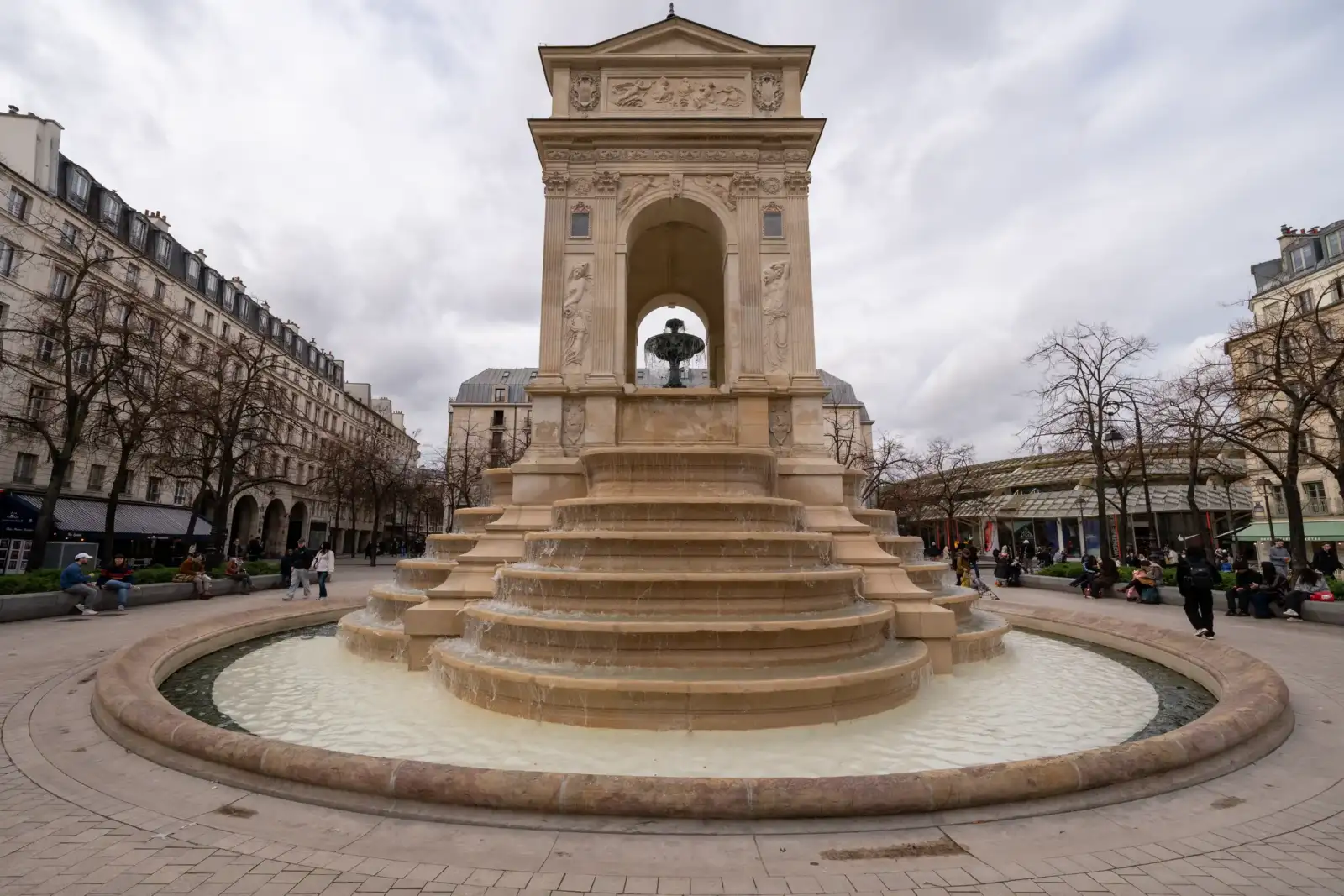 La fontaine des Innocents à Paris avec ses gradins en pierre sous un ciel nuageux.