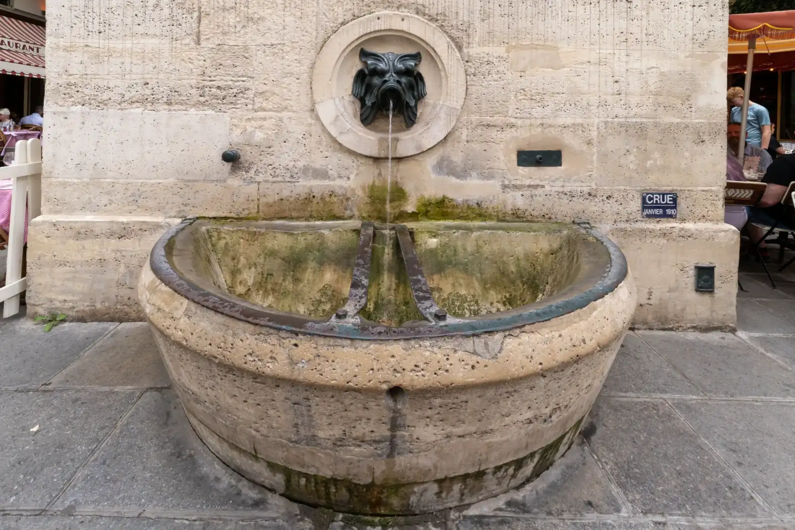 Une fontaine en pierre murale avec un masque de monstre crachant de l'eau.