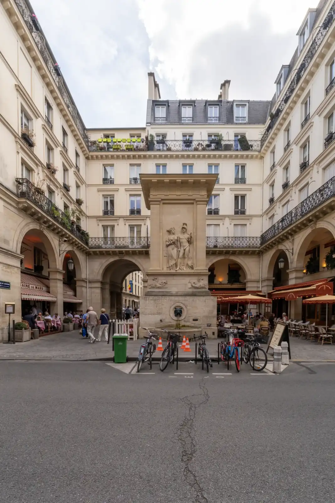 Une grande fontaine sculptée au milieu d une place parisienne entourée de beaux immeubles anciens.