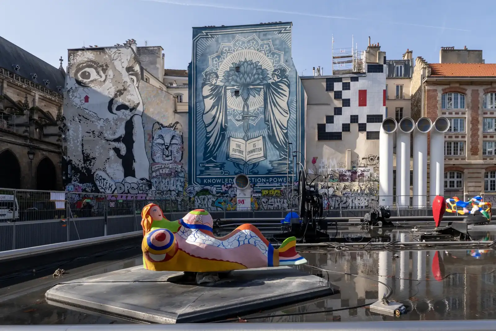 Une fontaine Stravinsky colorée se dresse devant des immeubles parisiens ornés de grandes fresques murales.