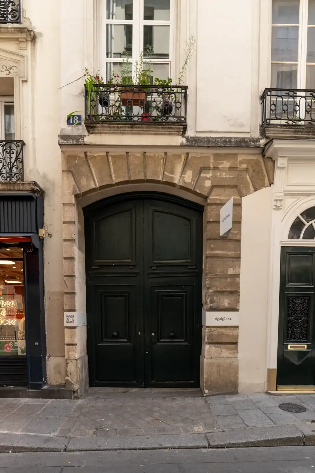 Façade parisienne avec une grande porte cochère noire encadrée de pierre et une enseigne discrète.